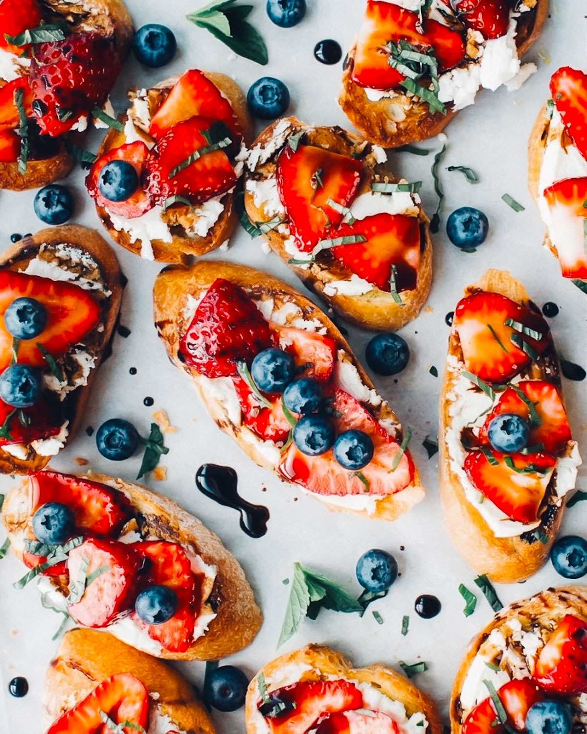 Red, white and blue 4th of july crostini appetizers on a tray with blueberries and strawberries.