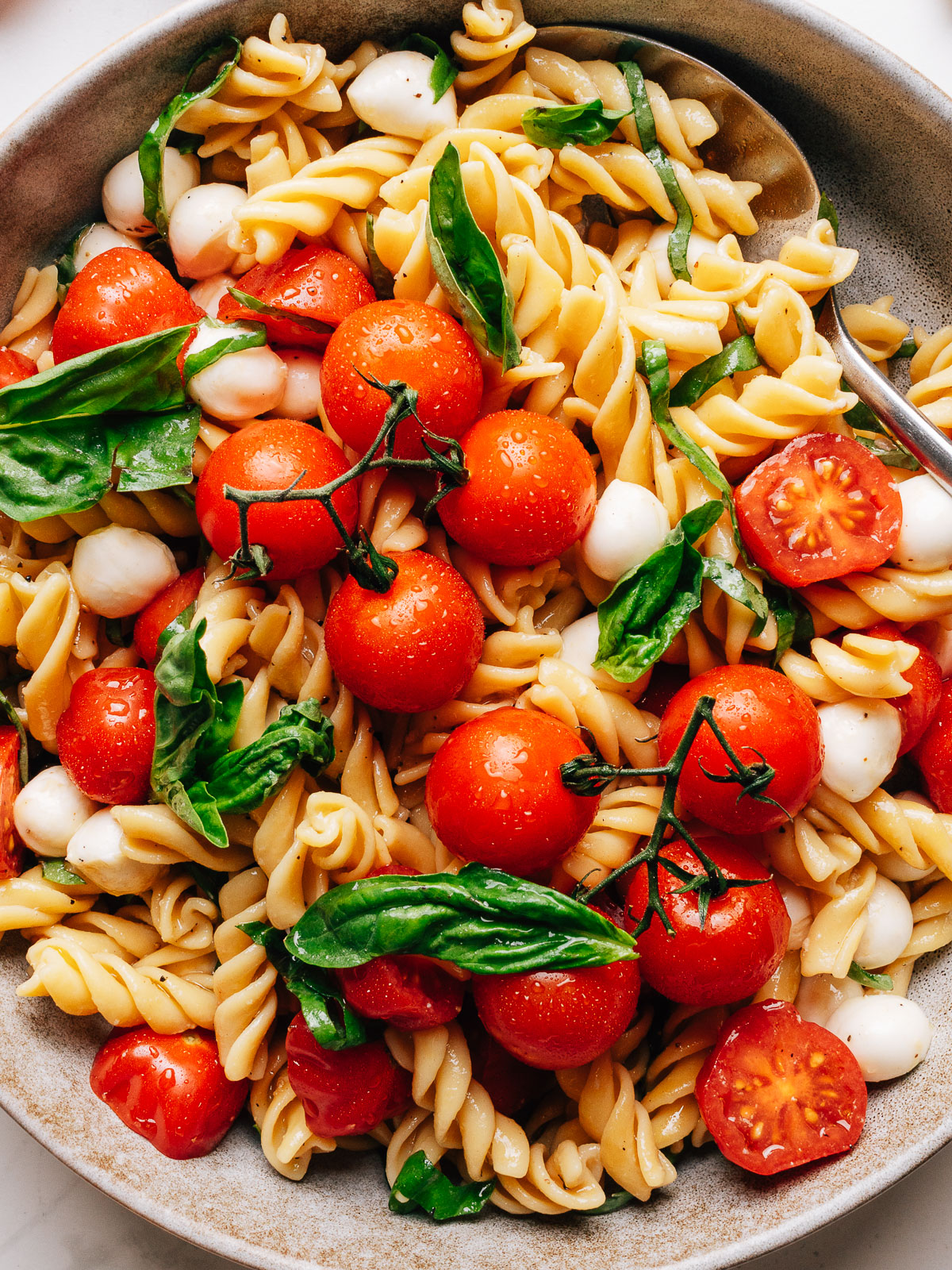 Caprese pasta salad in a bowl with cherry tomatoes, fresh mozzarella, and basil.