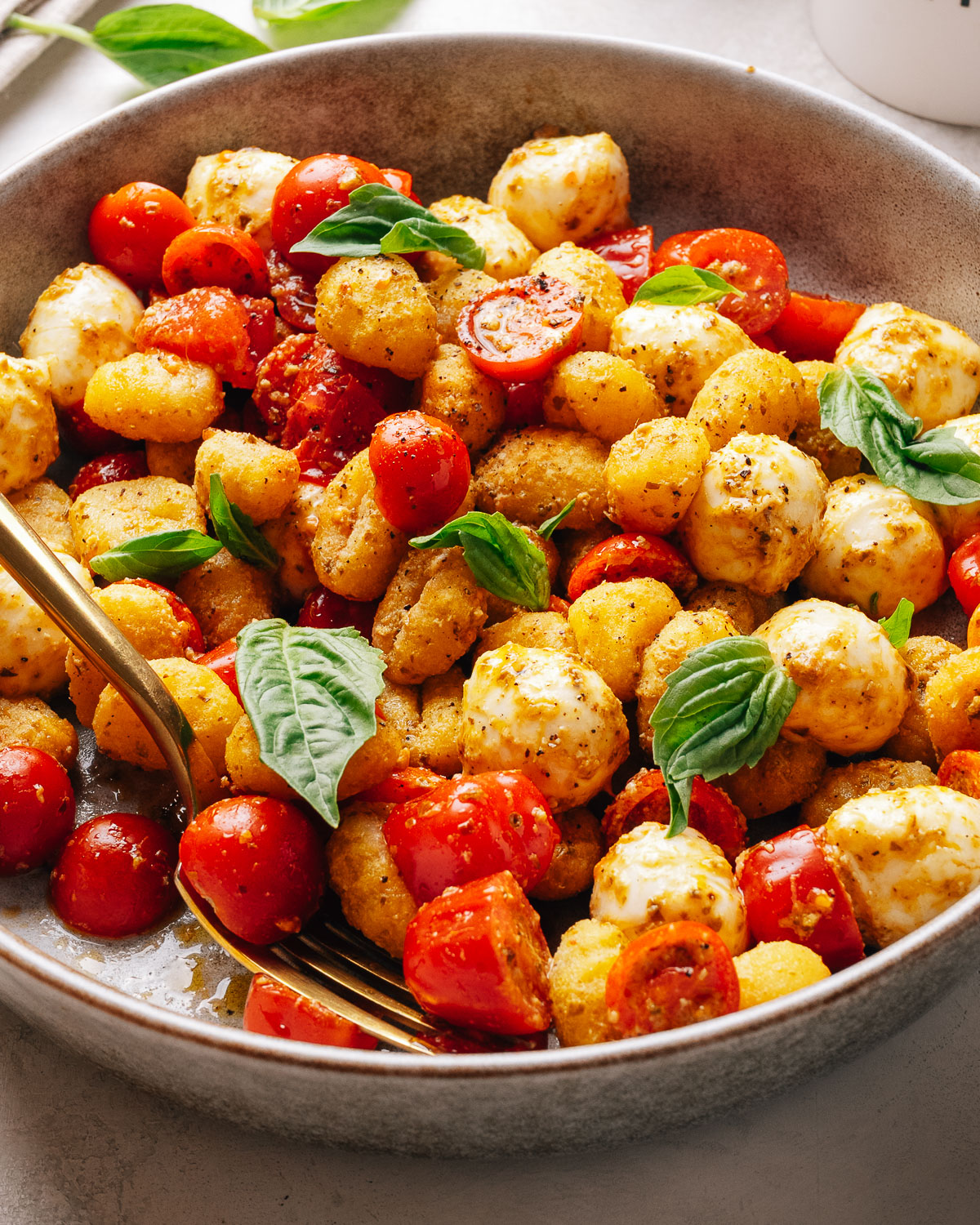 Overhead bowl of crispy gnocchi salad tossed with pesto and cherry tomatoes.