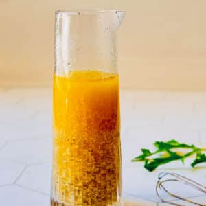 Dijon vinaigrette in a jar with a whisk resting beside it.