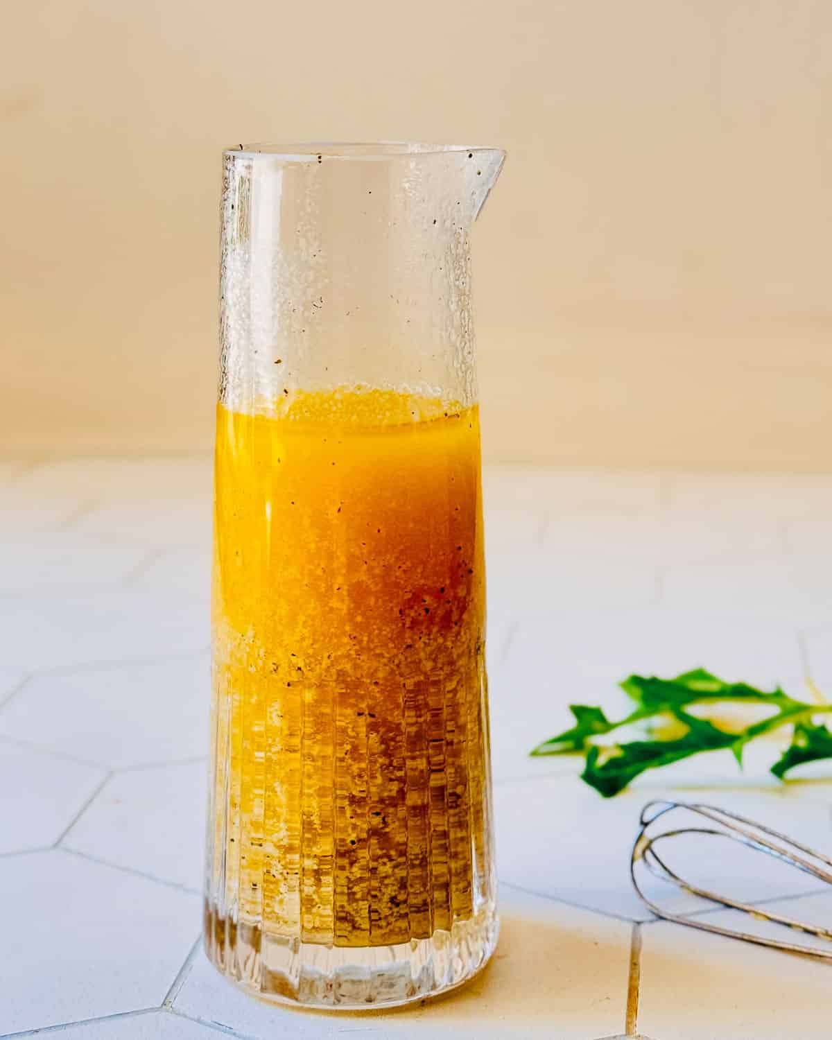 Dijon vinaigrette in a jar with a whisk resting beside it.