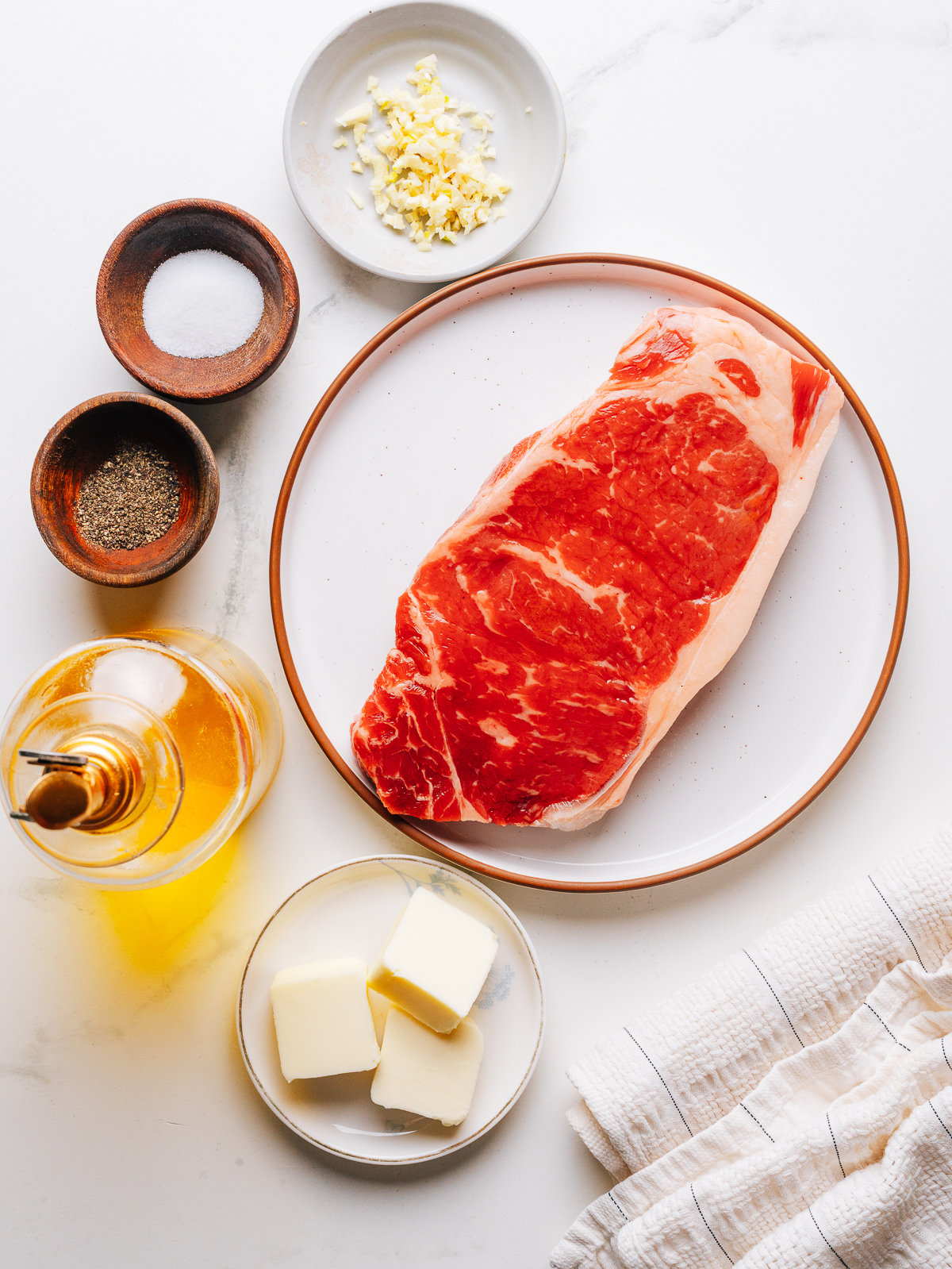 Raw steak with garlic, kosher salt, and black pepper laid out for garlic butter steak.
