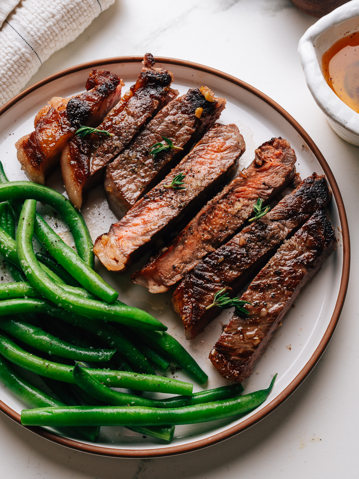 Sliced garlic butter steak on a plate with green beans and a dish of garlic butter.