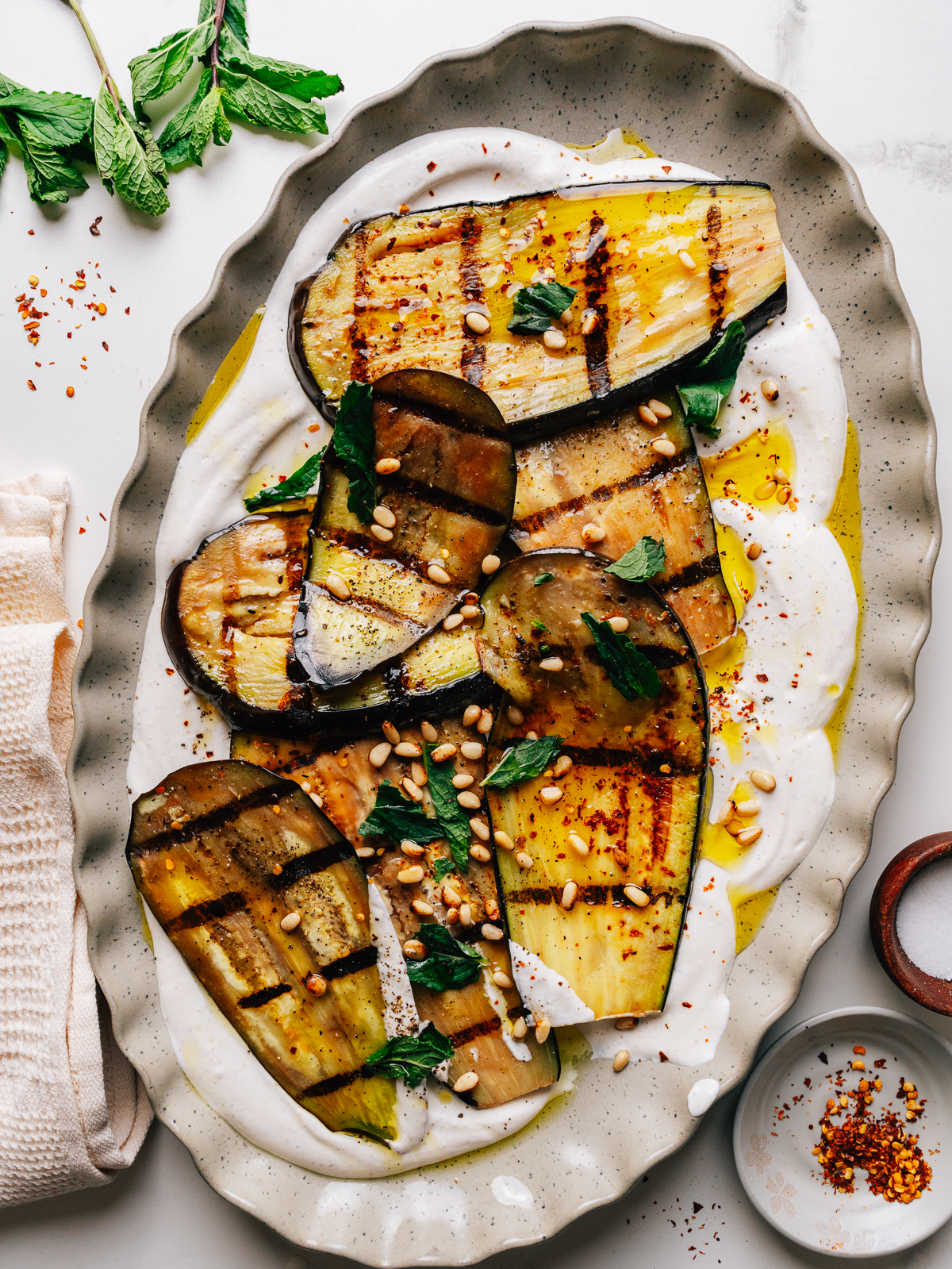 Grilled eggplant strips arranged over whipped feta with mint and pine nuts on a platter.