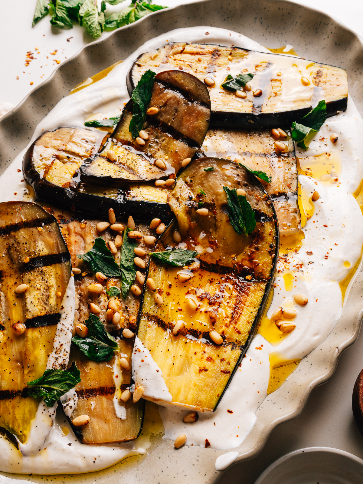 Grilled eggplant slices arranged over whipped feta with mint and pine nuts on a platter.
