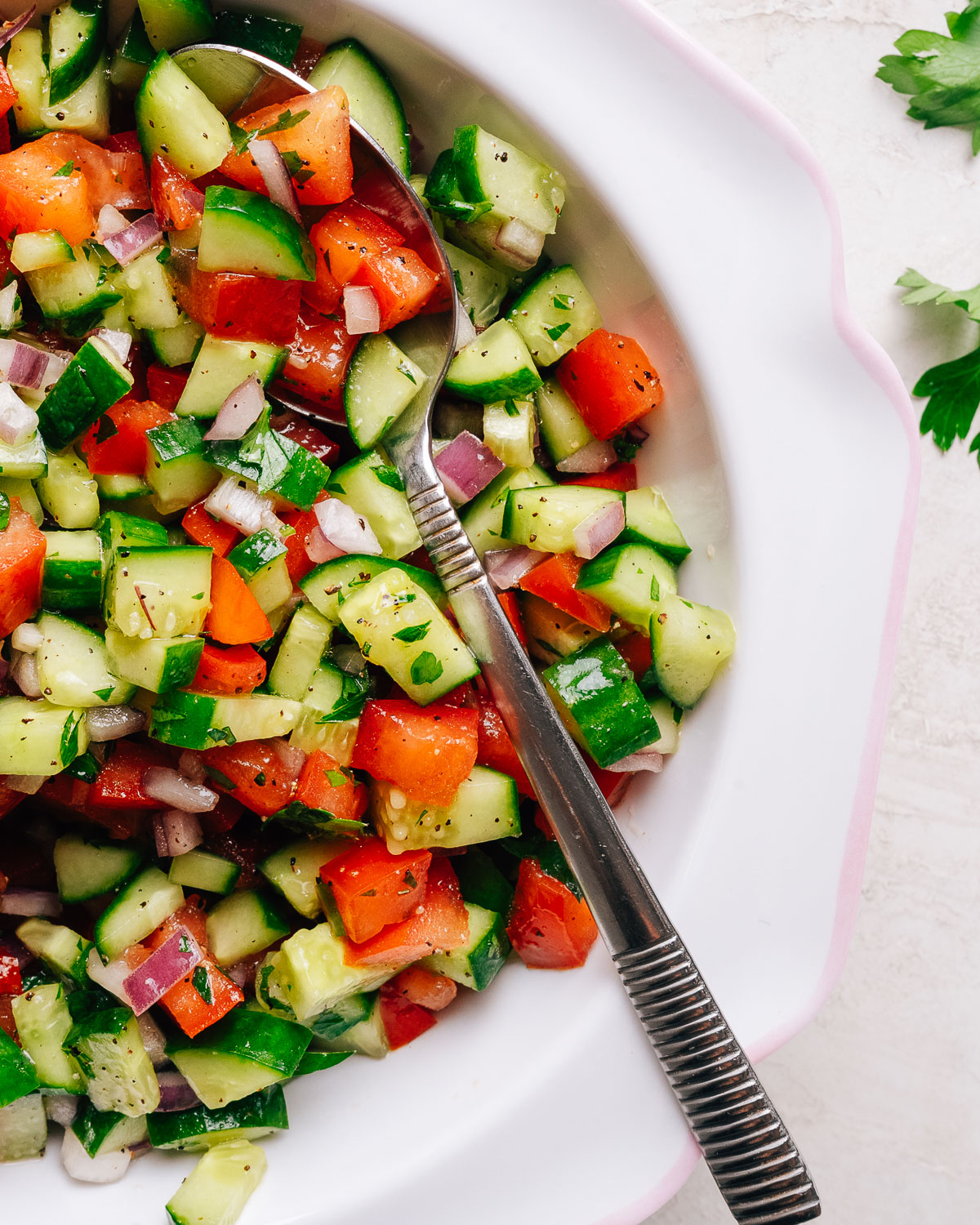 Close-up of fresh Israeli chopped salad tossed with herbs and a spoon.