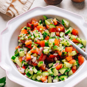 Israeli salad with diced cucumber, tomato, and red onion in a white bowl.