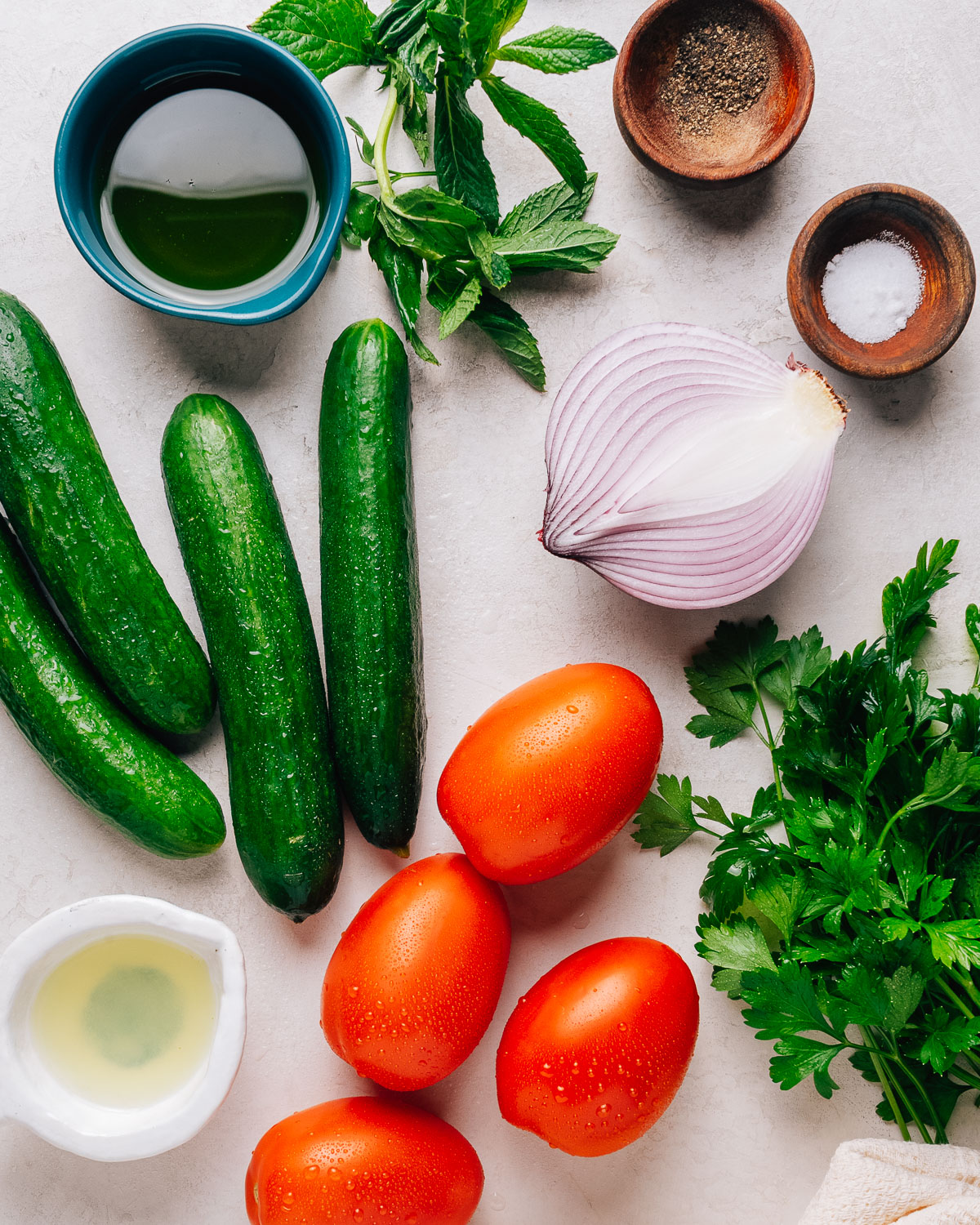 Ingredients for Israeli salad: cucumbers, tomatoes, red onion, parsley, mint, olive oil, and lemon.