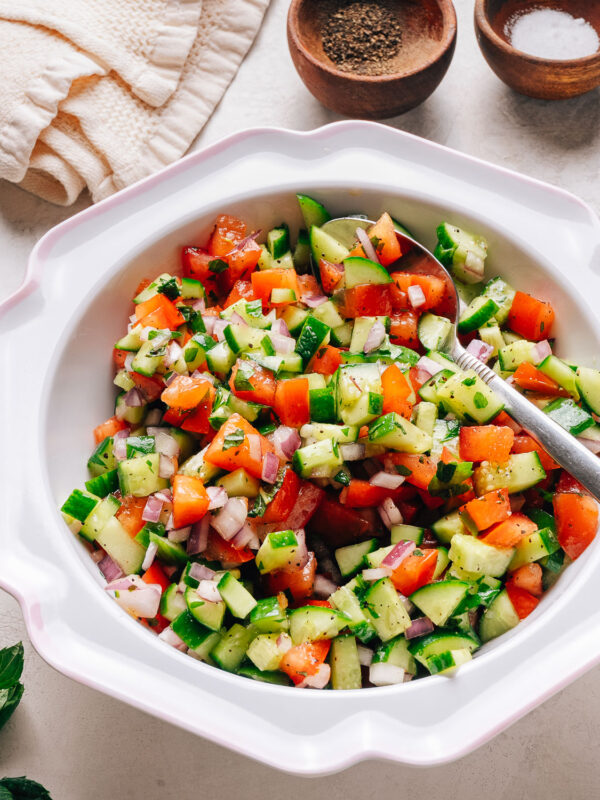 Israeli salad with diced cucumber, tomato, and red onion in a white bowl.