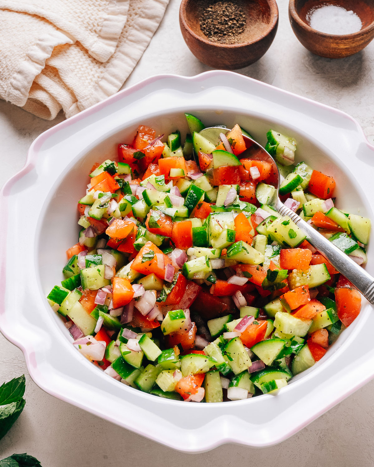 Israeli salad with diced cucumber, tomato, and red onion in a white bowl.