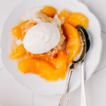 Overhead bowl of peach cobbler with a scoop of vanilla ice cream.