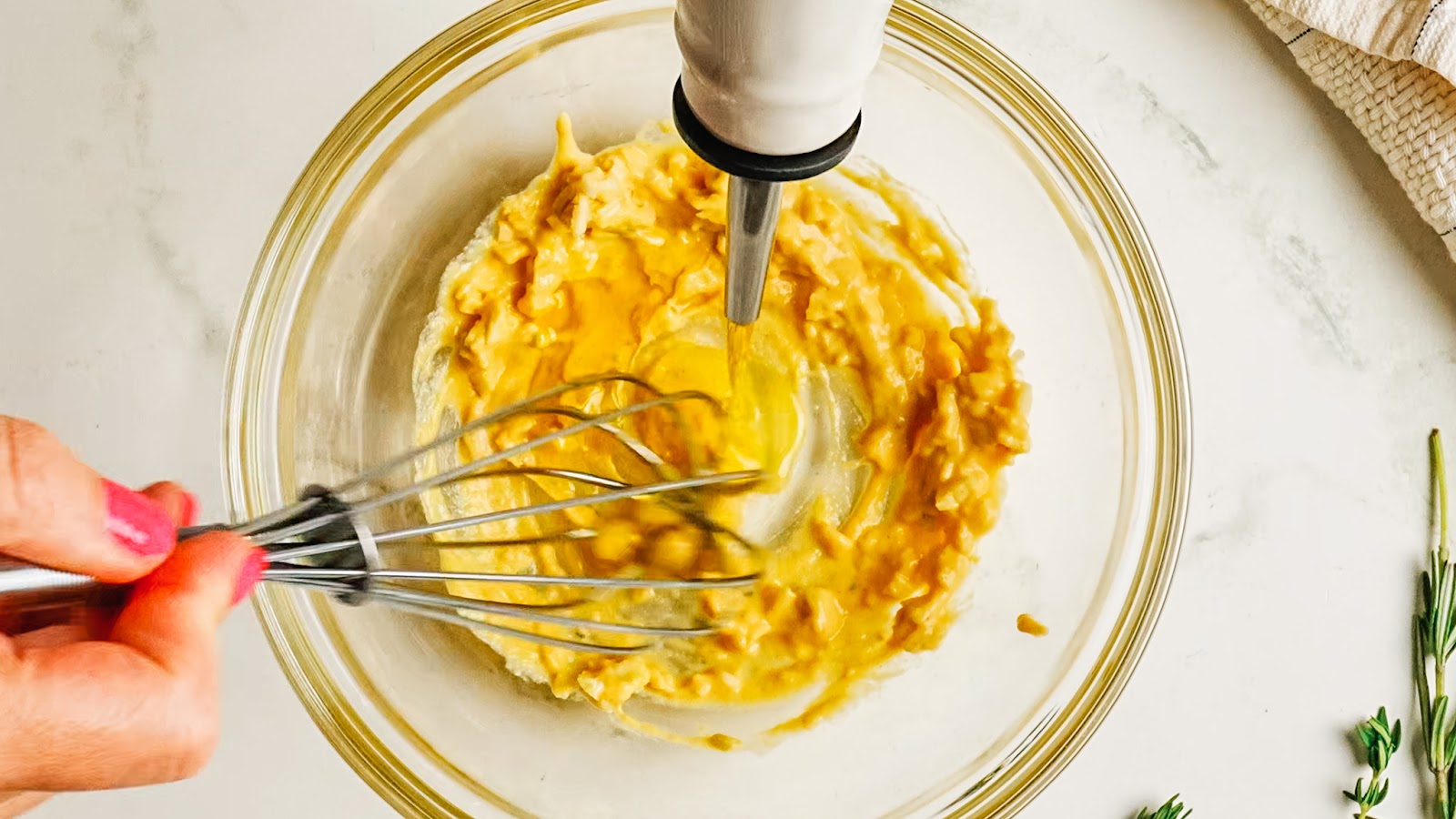 Streaming olive oil into the mustard while whisking to emulsify.