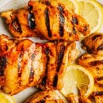 Grill-marked balsamic chicken thighs on a white plate garnished with fresh lemon slices.