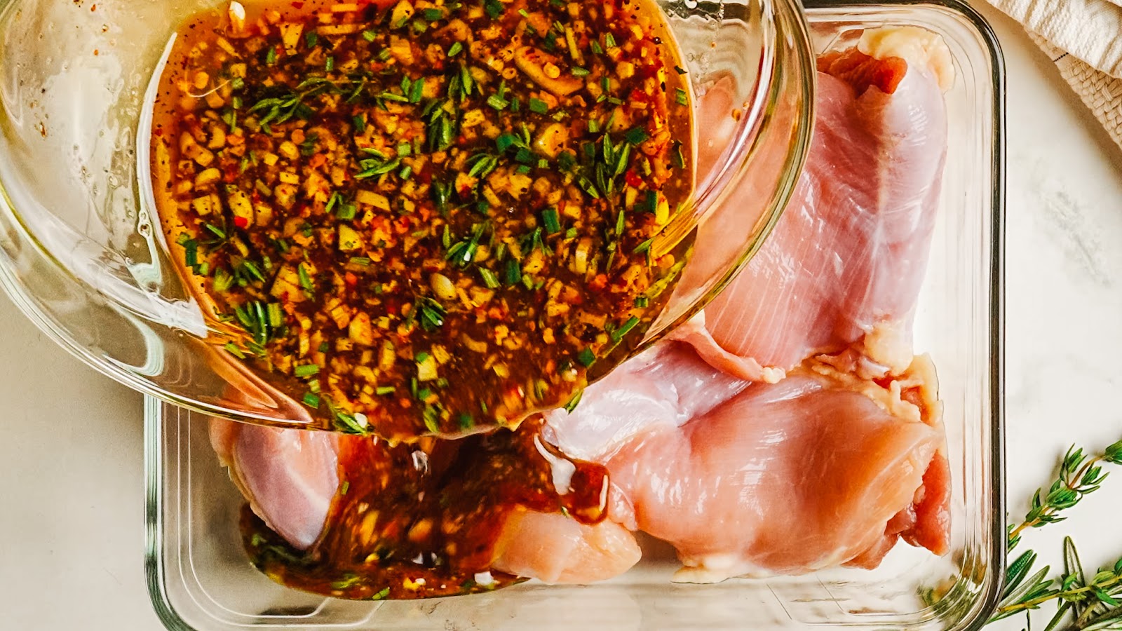 Pouring balsamic marinade over raw chicken thighs in a dish.