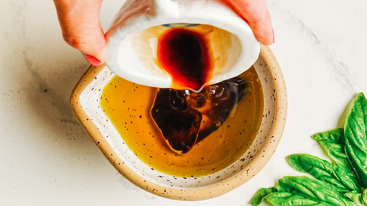 Pouring balsamic vinegar into olive oil to start the vinaigrette.