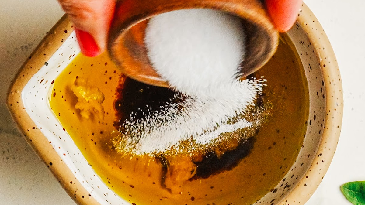 Adding salt and pepper to the balsamic vinaigrette in a bowl.