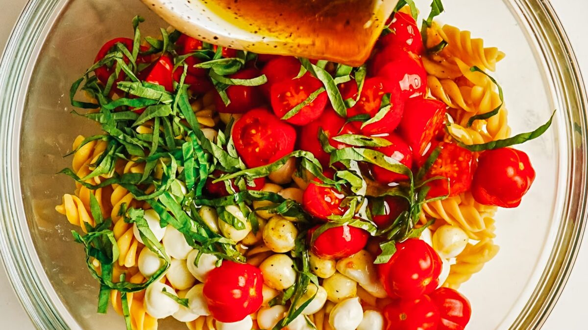 Balsamic dressing poured over caprese pasta salad before tossing.