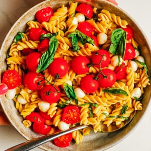 Caprese pasta salad in a bowl with cherry tomatoes, fresh mozzarella, and basil.