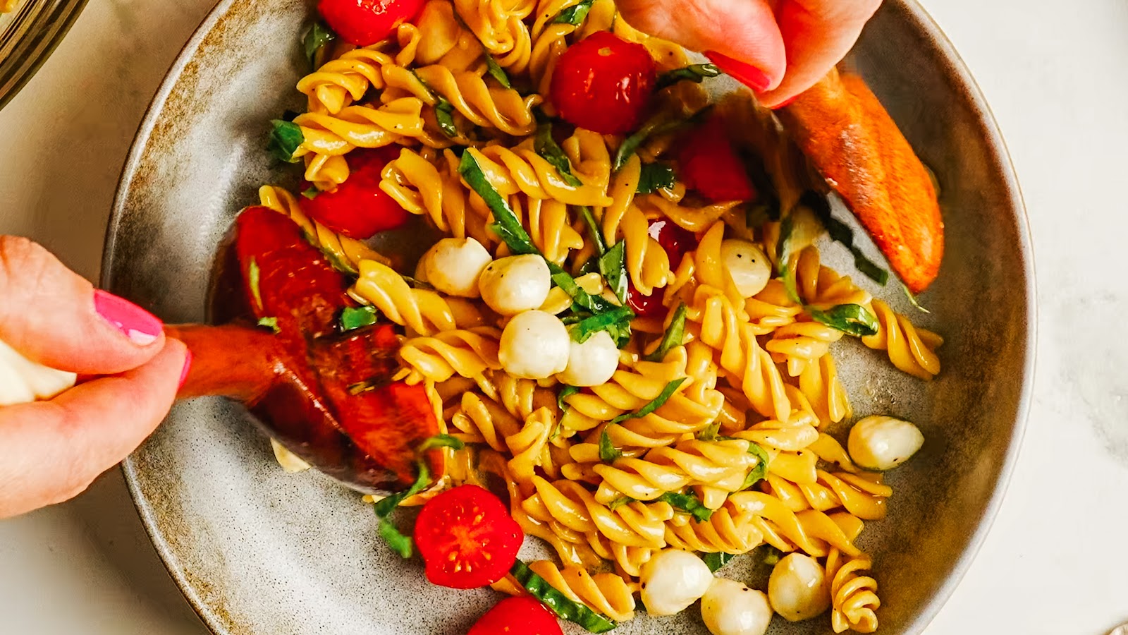 A served portion of caprese pasta salad with wooden servers.