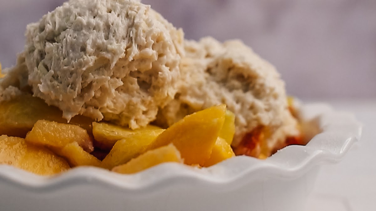 Easy peach cobbler with a golden biscuit topping in a white baking dish.