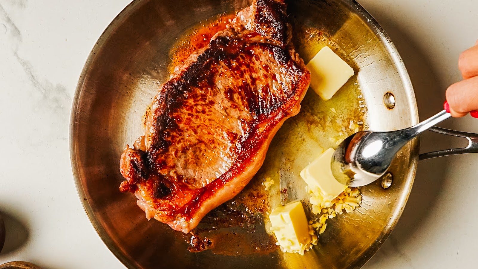 Spooning foaming garlic butter over the steak in the pan.