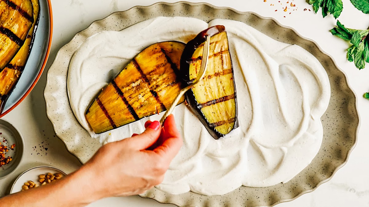 Arranging grilled eggplant over whipped feta on a platter.