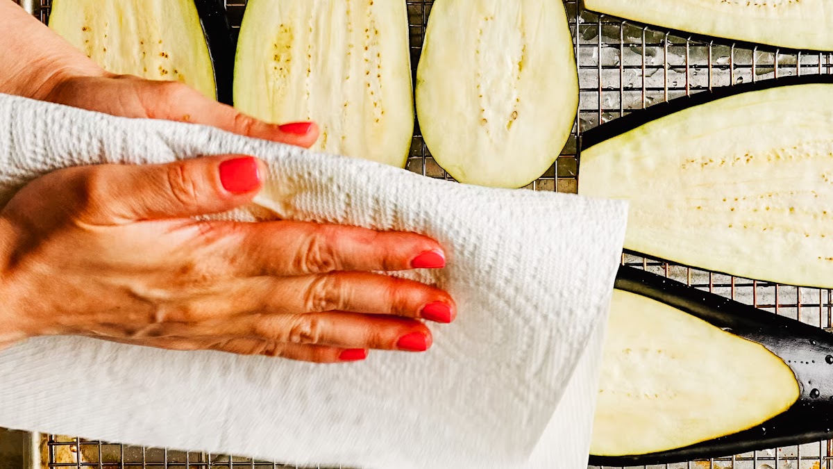 Pressing salted eggplant slices dry with a paper towel.