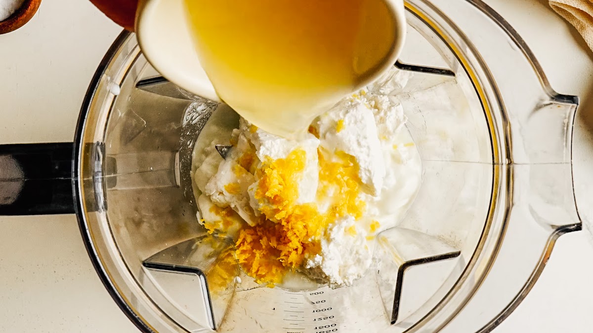Pouring olive oil into a blender with feta and yogurt for whipped feta.
