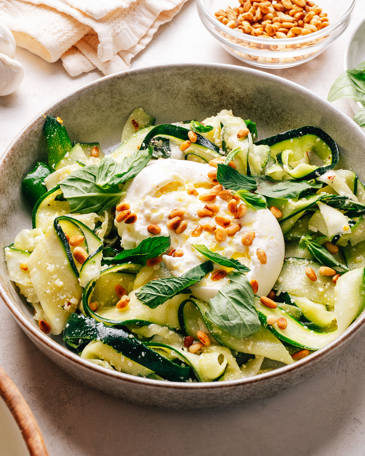 Zucchini salad with creamy burrata, toasted pine nuts, and fresh herbs in a bowl.