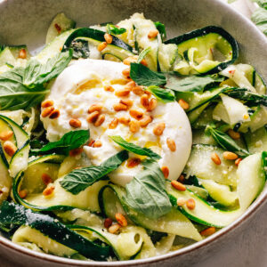 Zucchini salad with creamy burrata, toasted pine nuts, and fresh herbs in a bowl.