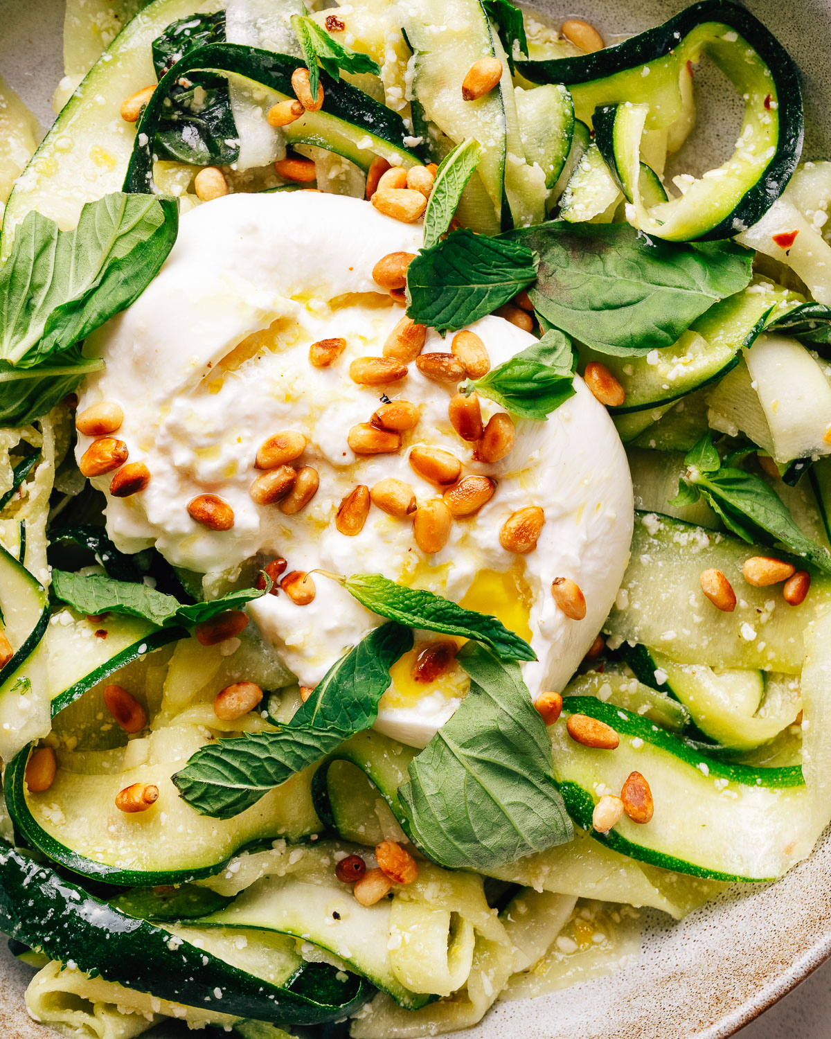 Zucchini salad with creamy burrata, toasted pine nuts, and fresh herbs in a bowl.
