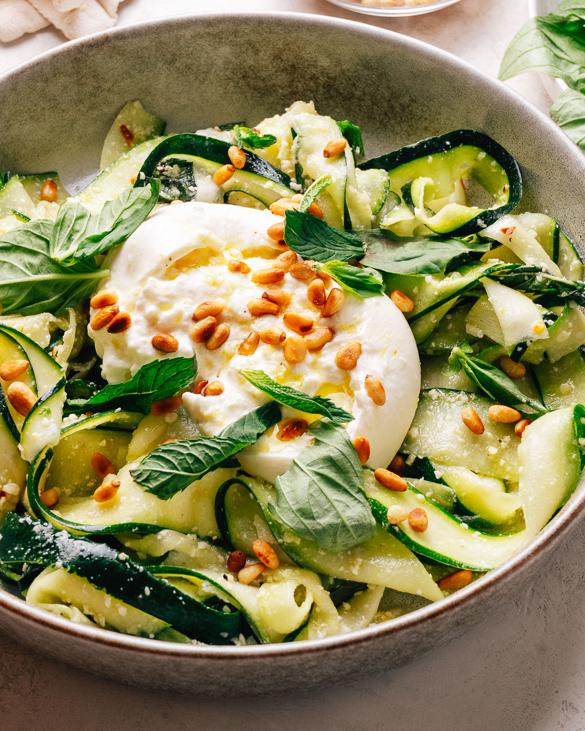 Zucchini salad with creamy burrata, toasted pine nuts, and fresh herbs in a bowl.