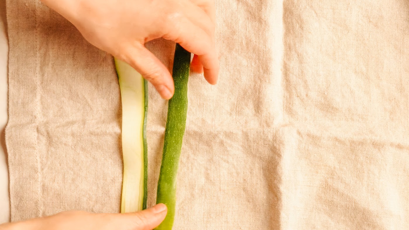 Blotting shaved zucchini ribbons dry on a tea towel.