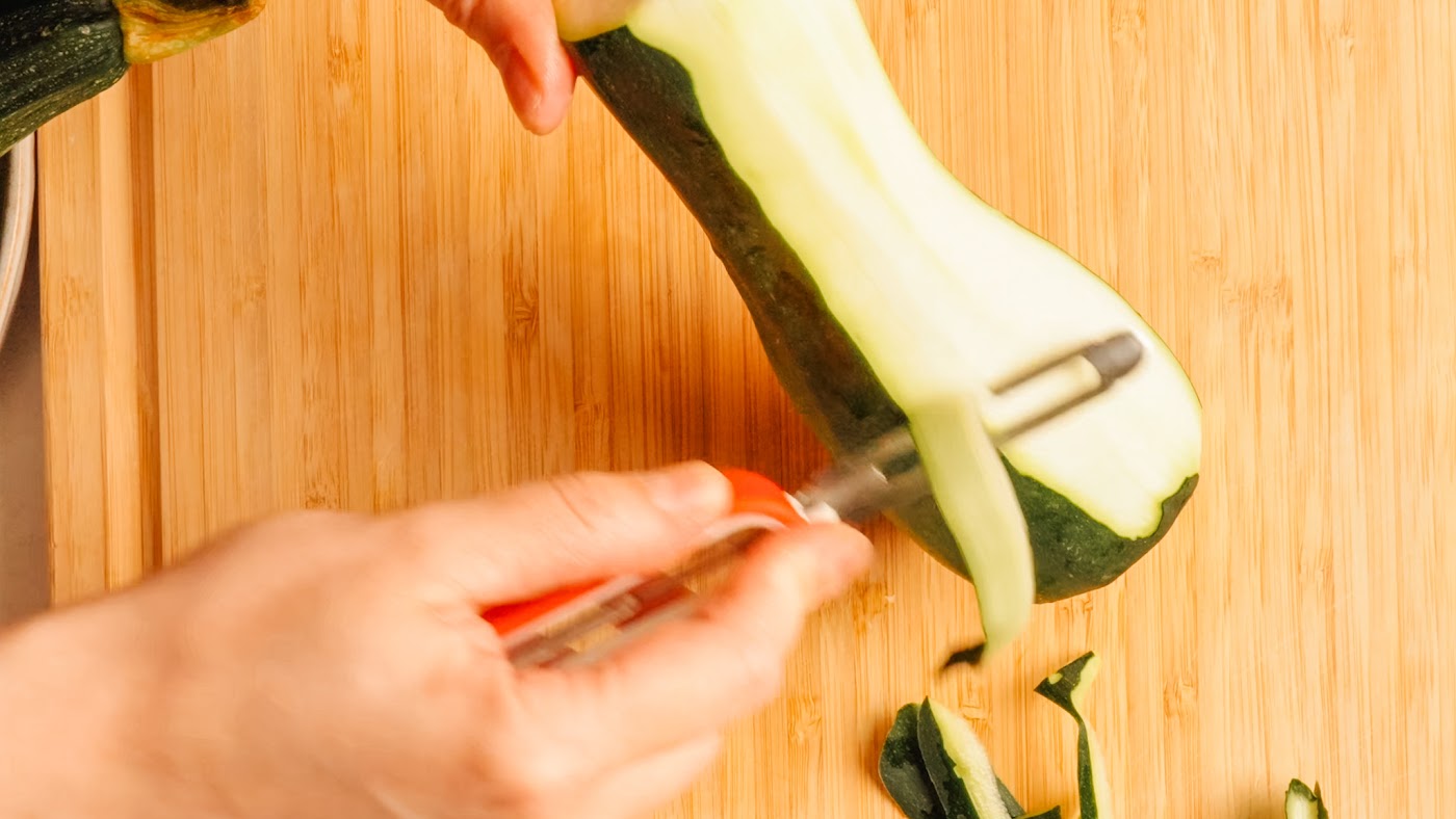 Shaving zucchini into thin ribbons with a vegetable peeler.