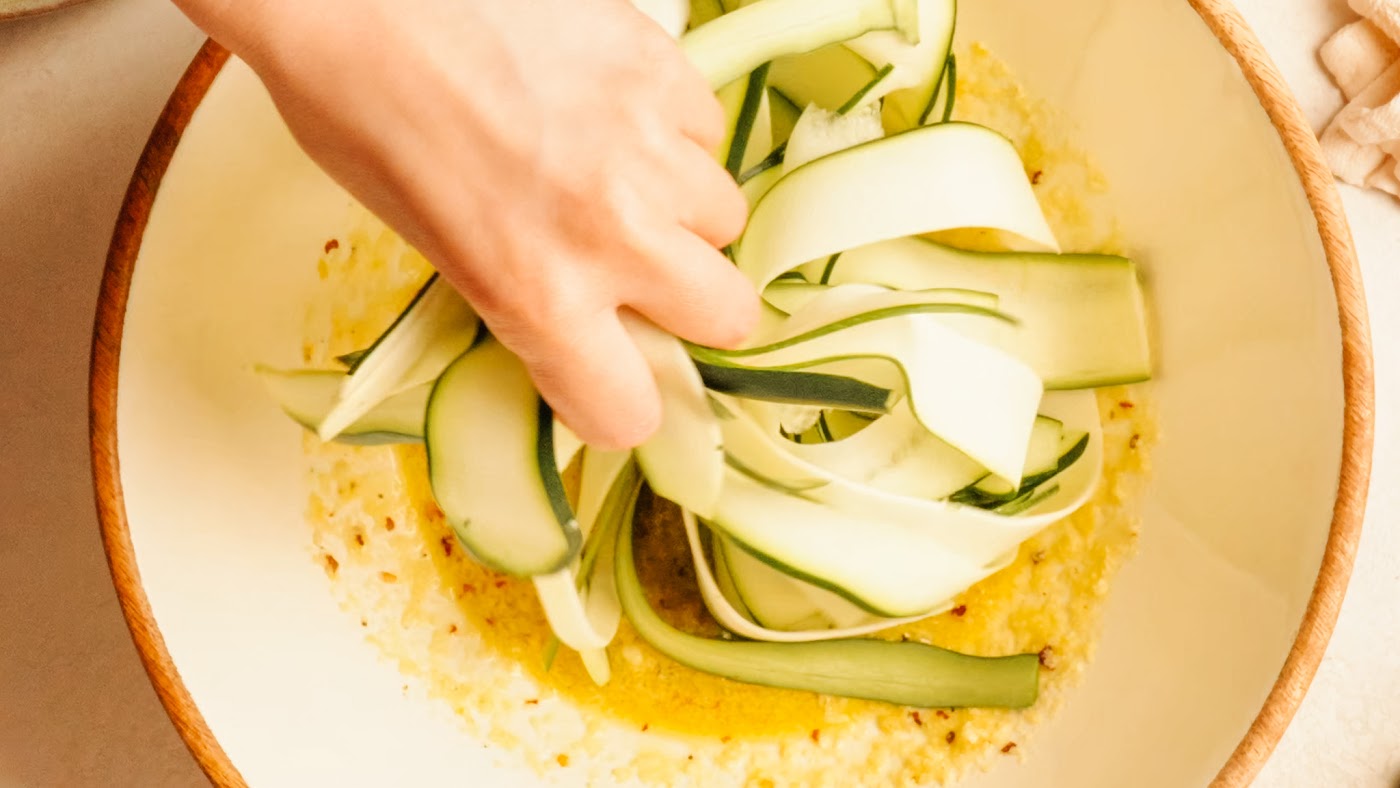 Tossing zucchini ribbons with dressing and fresh herbs.