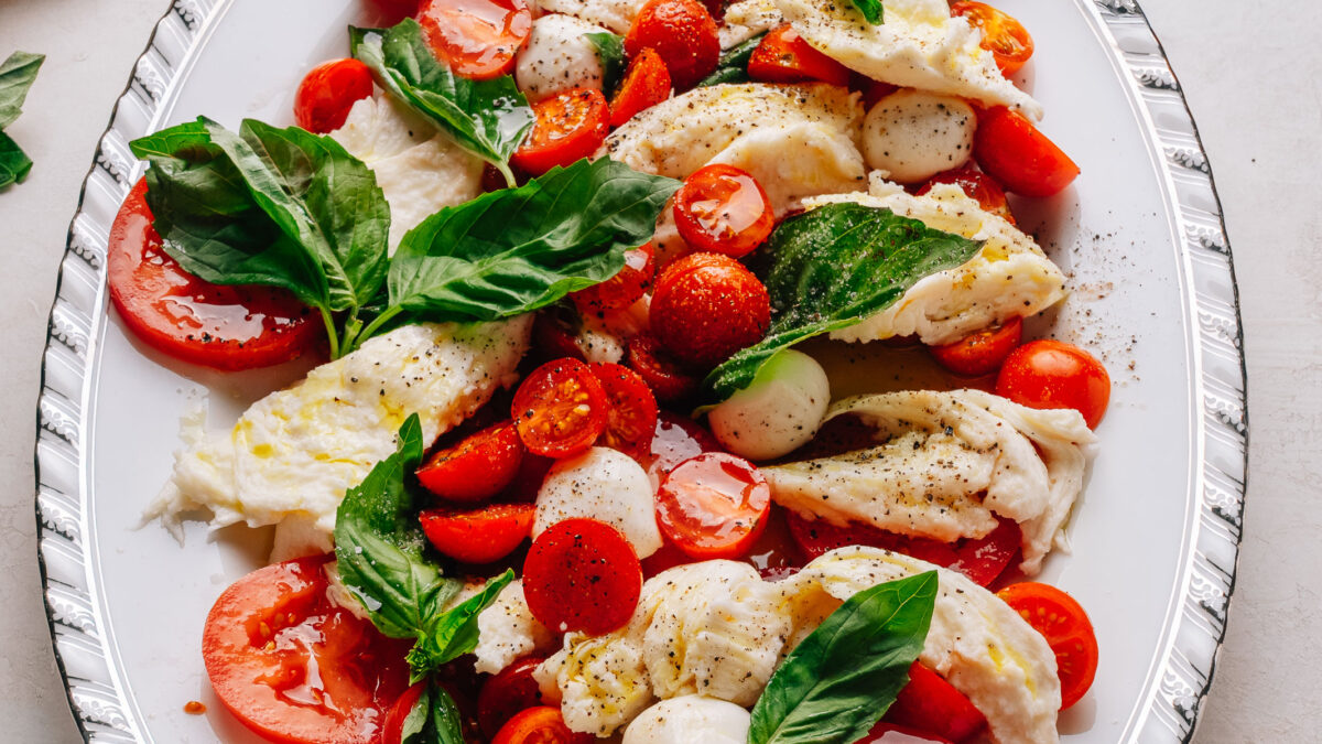 Caprese salad recipe with cherry tomatoes on a platter with torn mozzarella, ripe tomatoes and fresh basil.