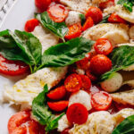 Caprese salad recipe with cherry tomatoes on a platter with torn mozzarella, ripe tomatoes and fresh basil.