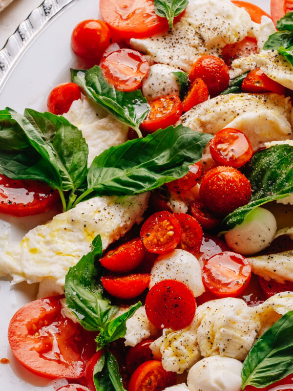 Caprese salad recipe with cherry tomatoes on a platter with torn mozzarella, ripe tomatoes and fresh basil.