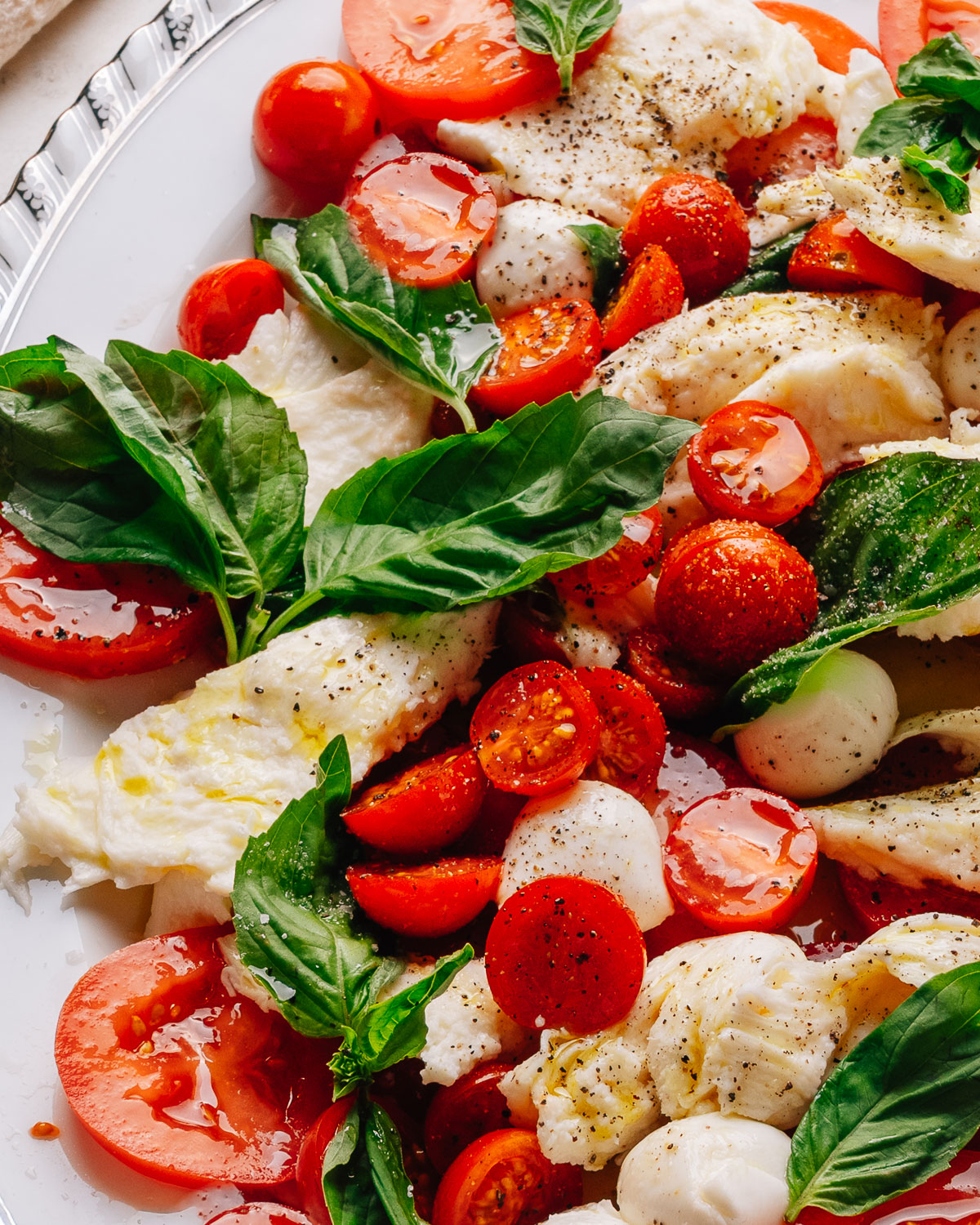 Caprese salad recipe with cherry tomatoes on a platter with torn mozzarella, ripe tomatoes and fresh basil.