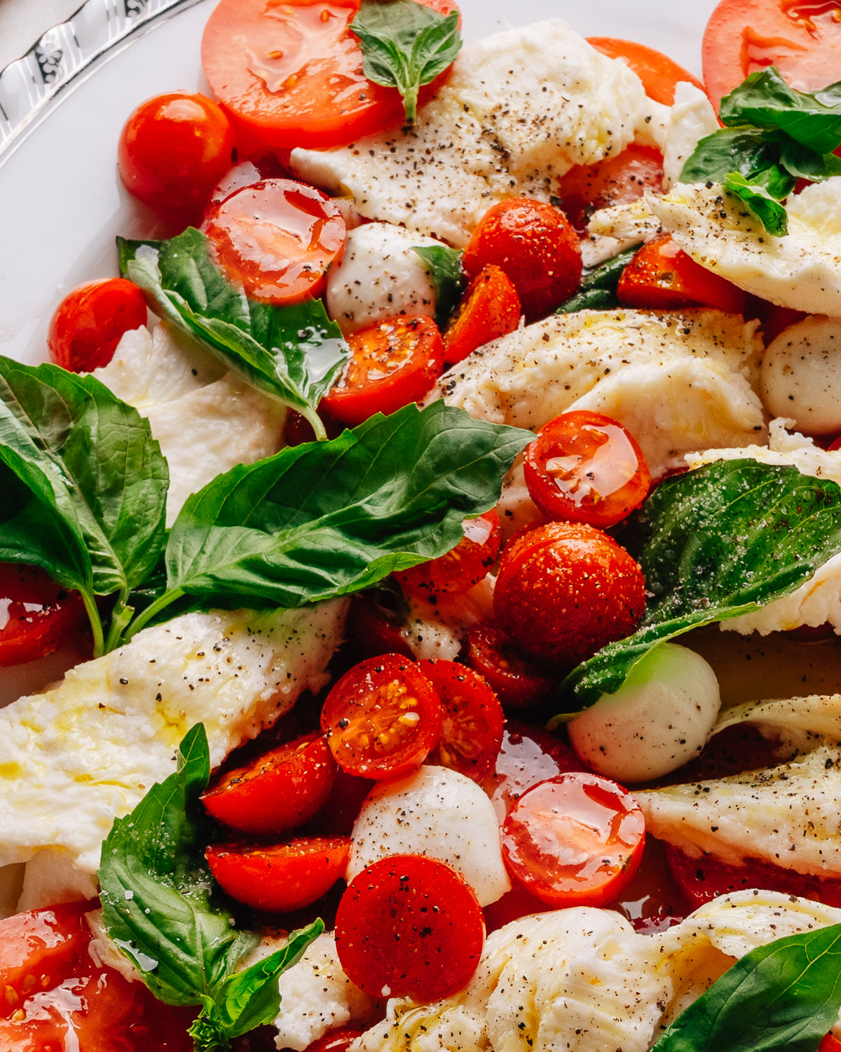 Caprese salad recipe with cherry tomatoes on a platter with torn mozzarella, ripe tomatoes and fresh basil.
