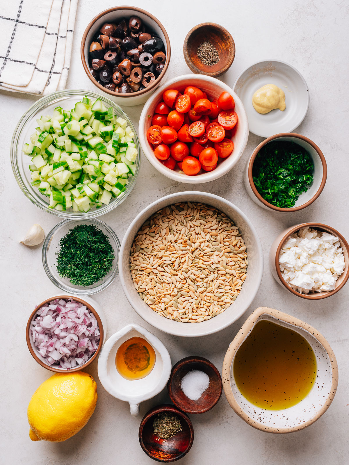 Orzo pasta salad ingredients with with cucumber, cherry tomatoes, olives and feta in a bowl.