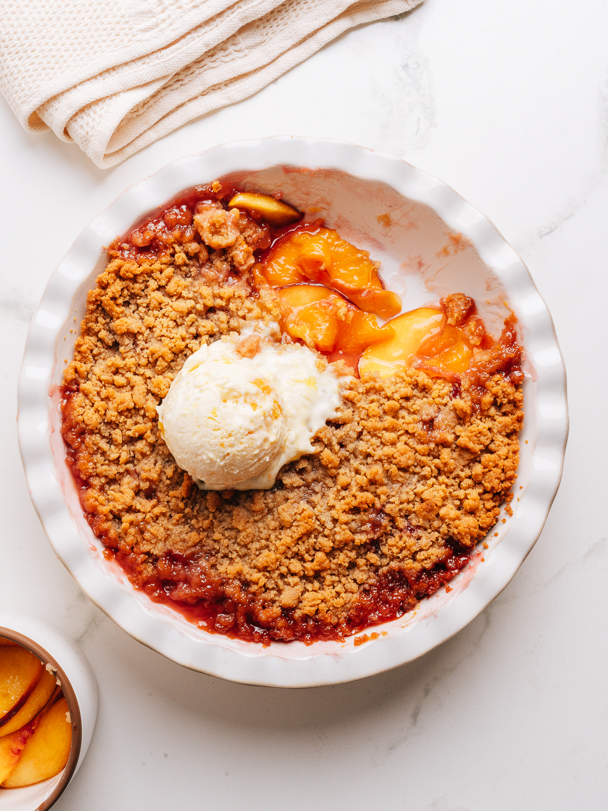 A pie dish of peach crumble with a scoop of vanilla ice cream.