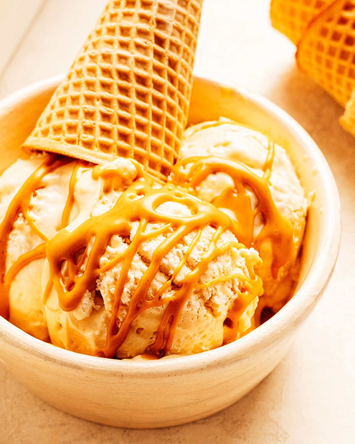 Scoops of homemade peanut butter ice cream in a bowl with peanut butter drizzled on top. 
