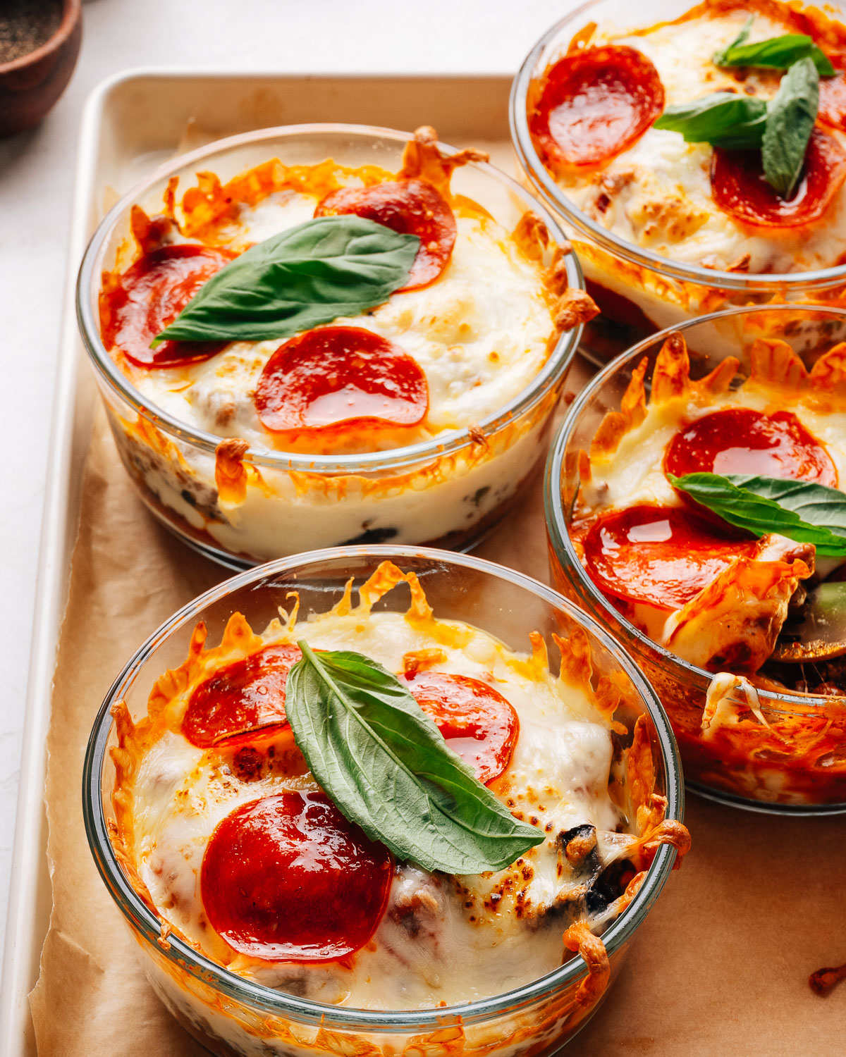 Pepperoni pizza bowls topped with fresh basil on a sheet pan.
