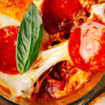 Pepperoni pizza bowls topped with fresh basil on a sheet pan.