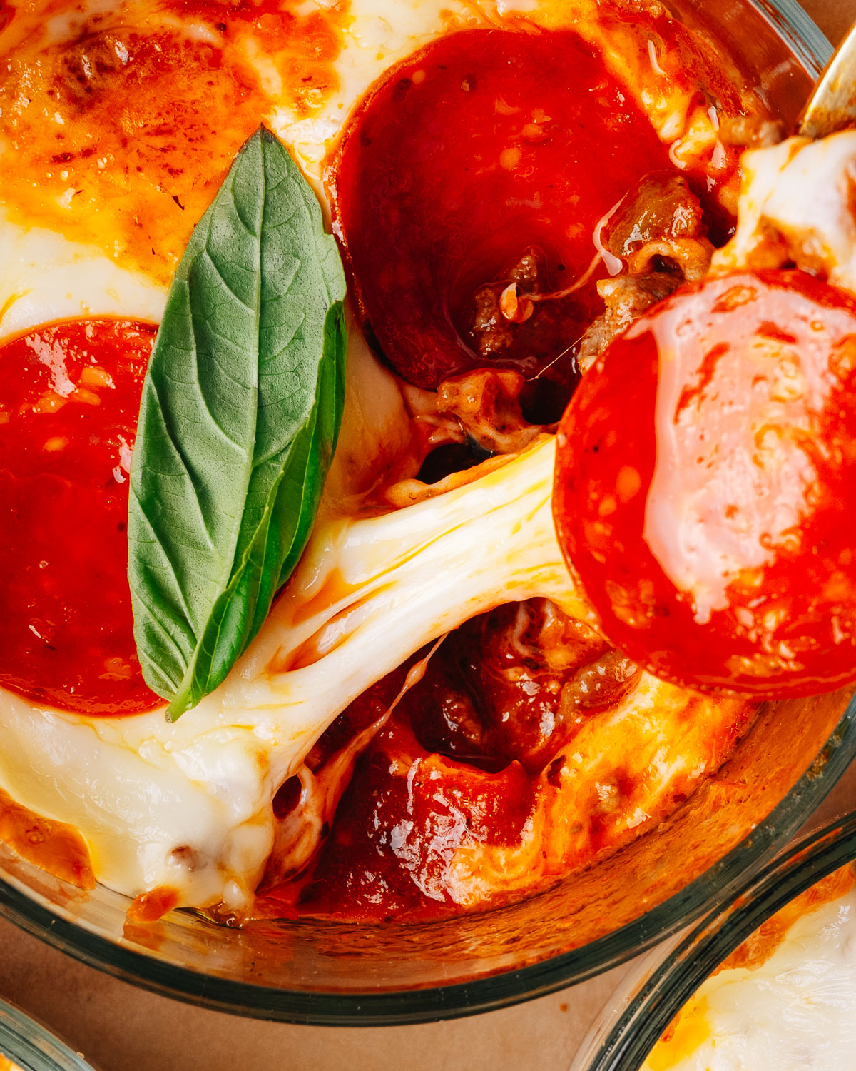Pepperoni pizza bowls topped with fresh basil on a sheet pan.