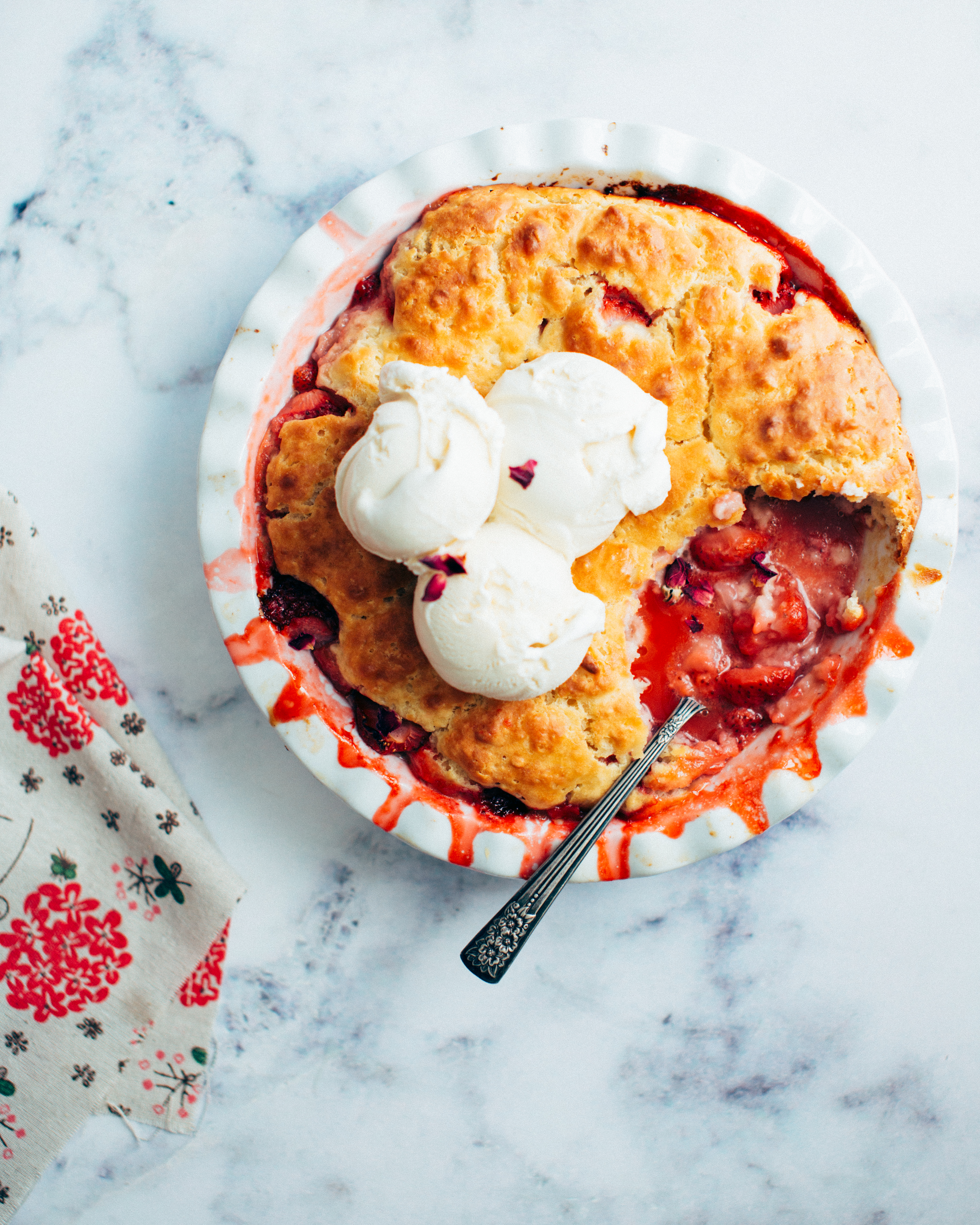 Baked strawberry cobbler with a spoonful removed and ice cream on top.